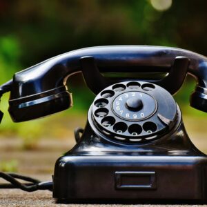 Close-up of a classic black rotary phone outdoors with a blurred green background.